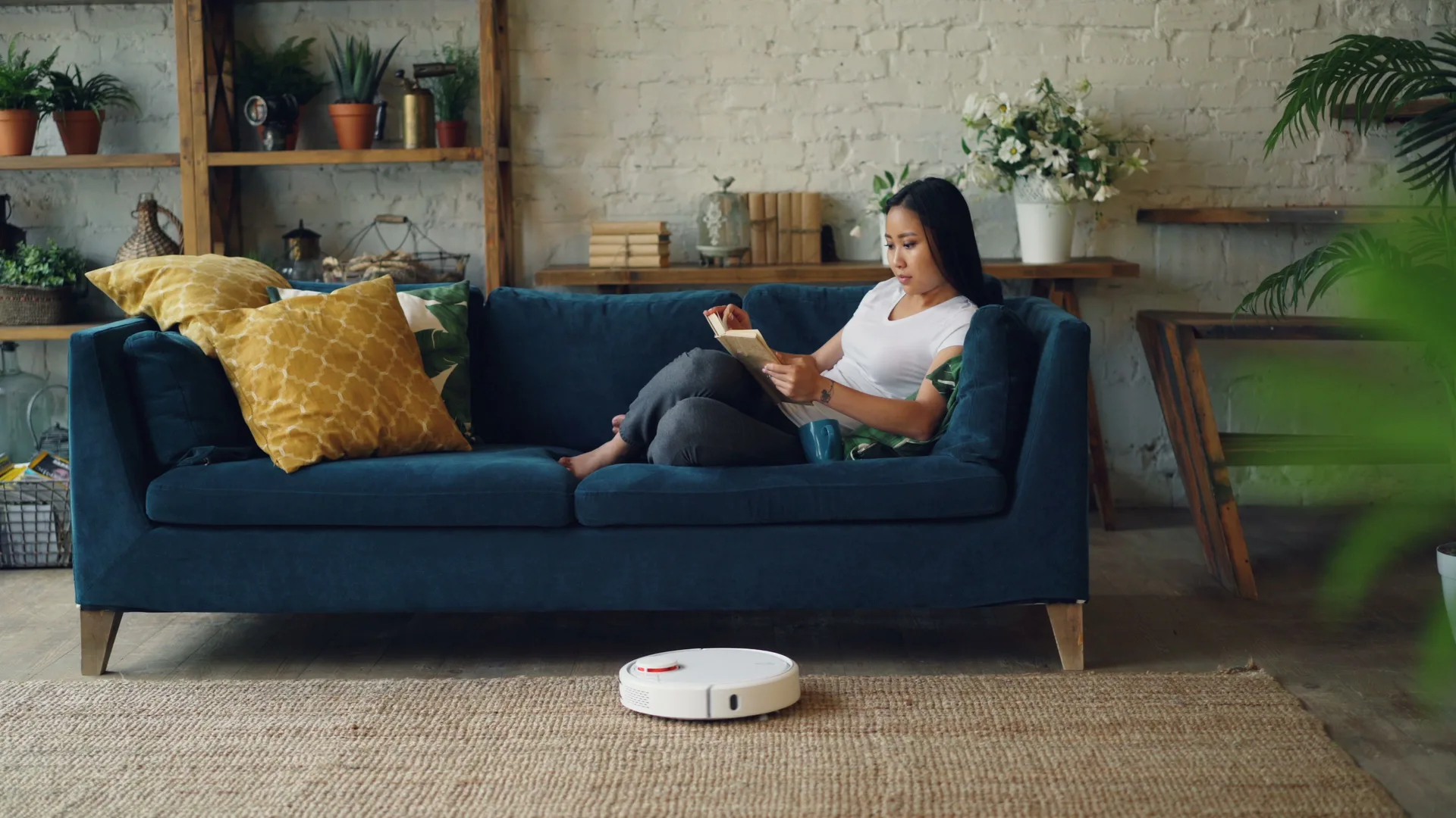 Living con una aspiradora robot limpiando la alfombra mientras una persona lee en el sofá
